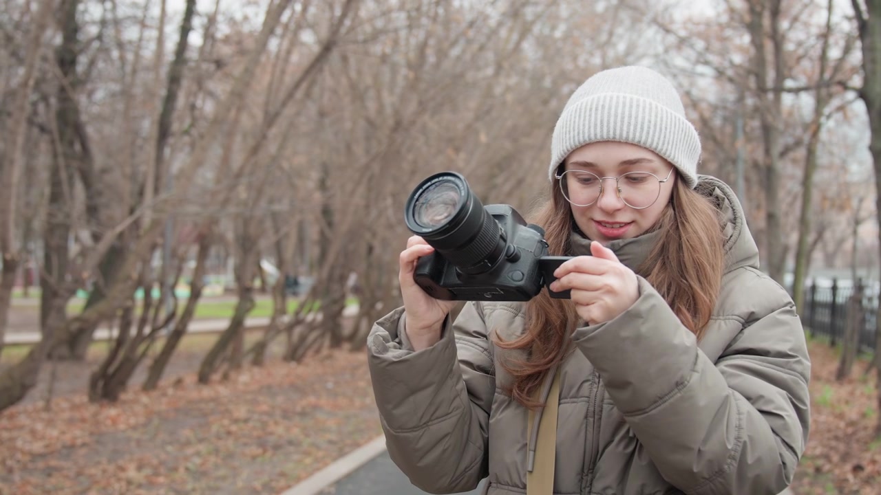 Woman reviewing photos on camera screen, scrolling playback and inspecting exposure, zooming into detail and adjusting settings, satisfied expression while checking shots along treelined lane