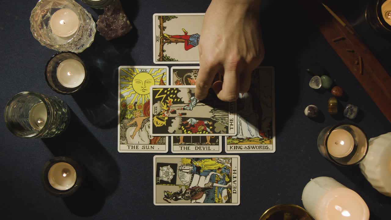 toma aérea de una persona que hace una lectura de cartas del tarot colocando cartas en la mesa con velas y cristales 5