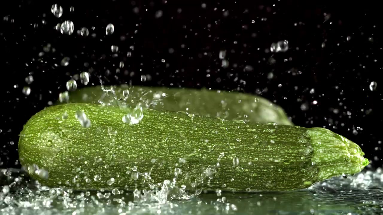 Zucchine verdi fresche con schizzi d'acqua su sfondo nero.