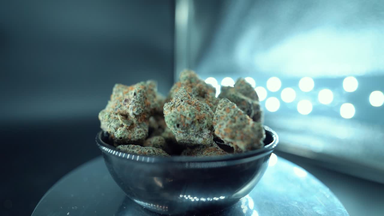 Una ripresa ravvicinata cinematografica, dettagliata e fluida di una pianta di cannabis, varietà ibride arancioni, tipo Indica, fiore di marijuana verde, slow motion a 120 fps, luci LED da studio, supporto rotante luminoso
