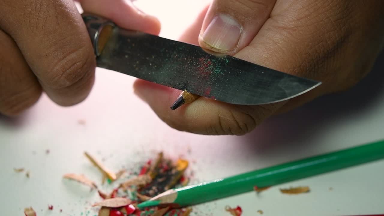 Opptak av hender som sakte spisser en blyant og noen fargeblyanter med en skarp kniv