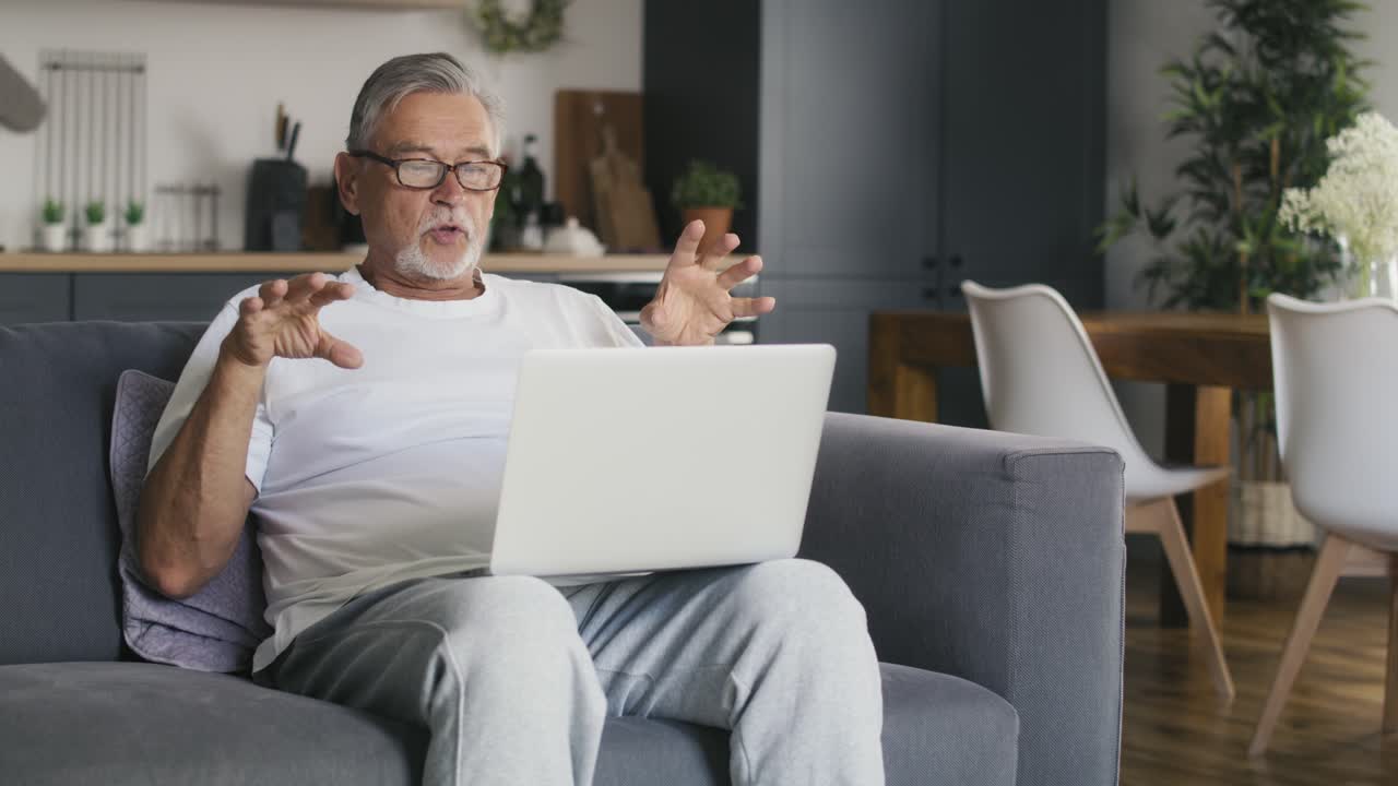 Senior caucasian man sitting at the couch and talking by video call.