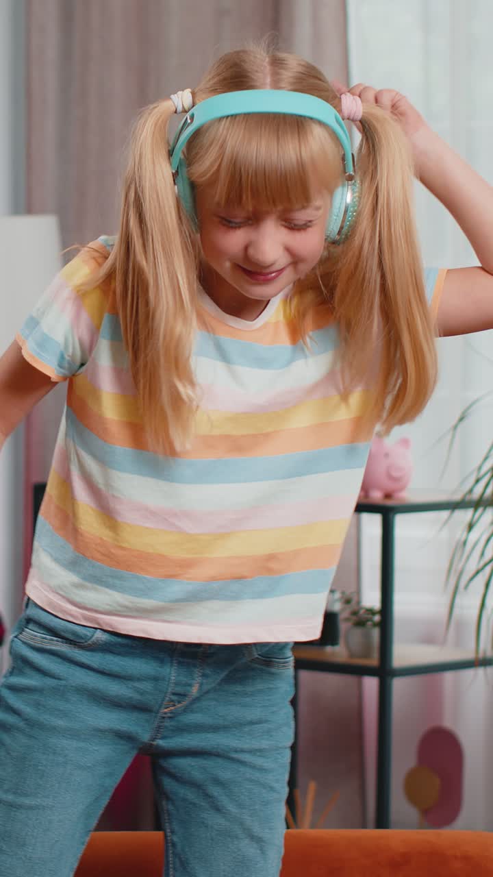 Happy teen lady in wireless headphones relaxing sitting on sofa at home listening favorite music