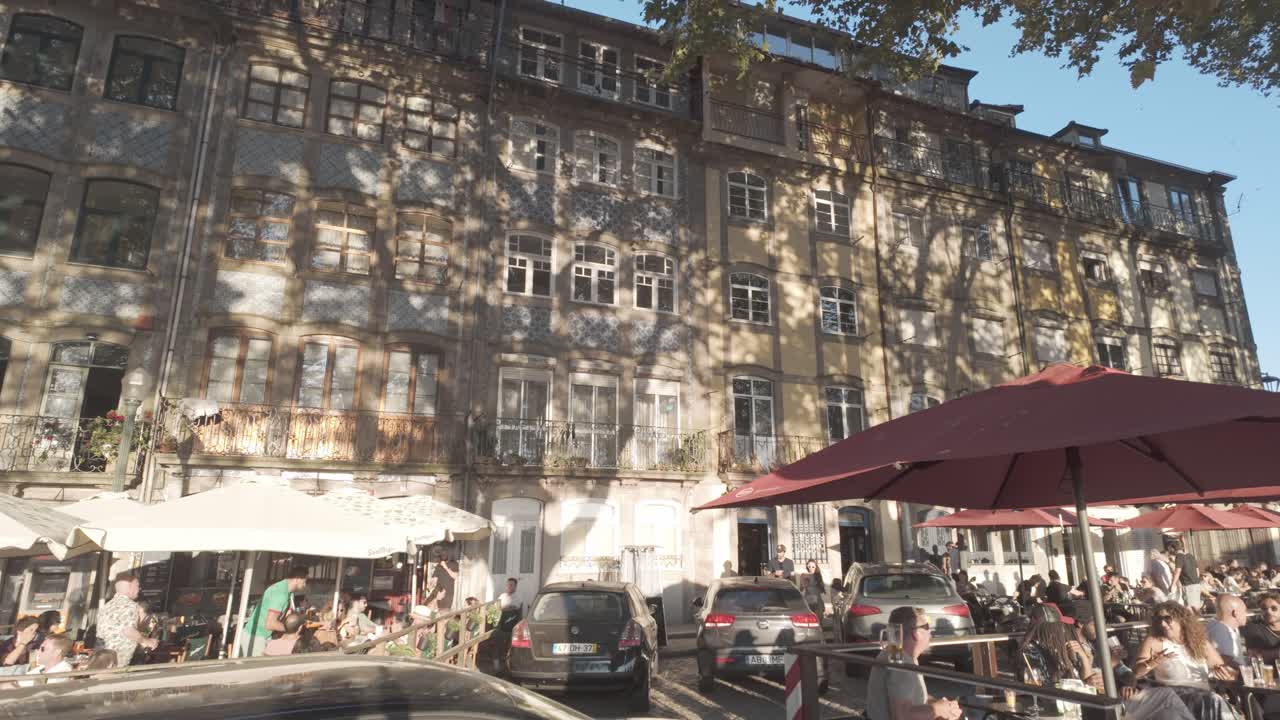 Old building and lively street with people dining at outdoor cafes in Porto during sunset