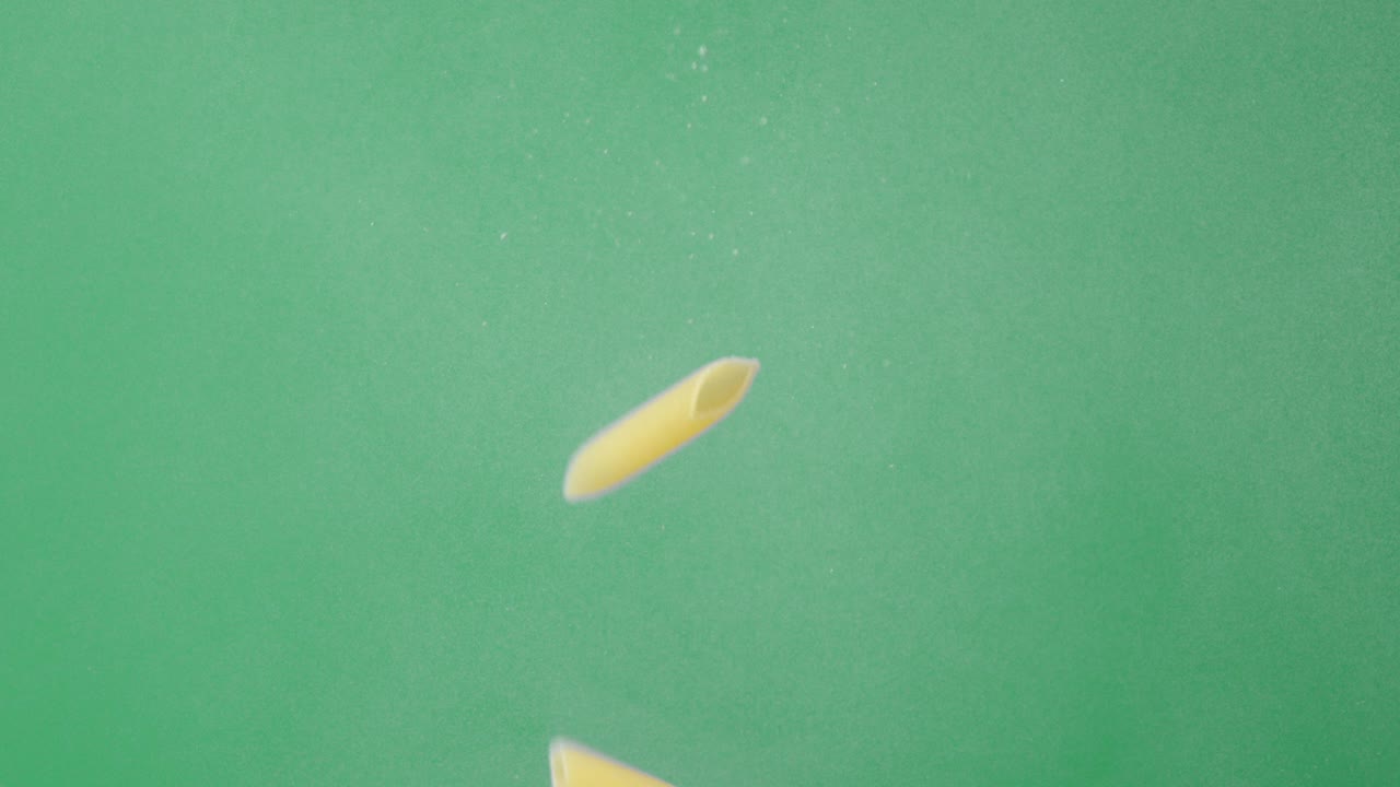 Dry penne pasta slowly falling under water with air bubbles.
