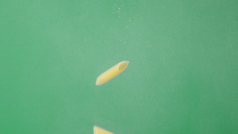 dry penne pasta slowly falling under water with air bubbles.