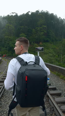 man hiking on train tracks with a smartphone