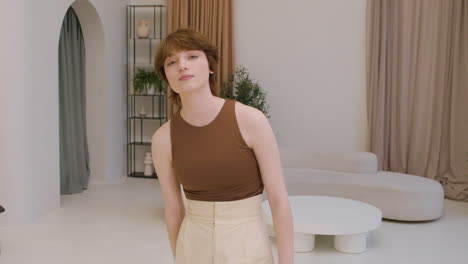 girl wearing elegant clothes standing in the middle of the living room in a modern house smiling and looking at the camera 1