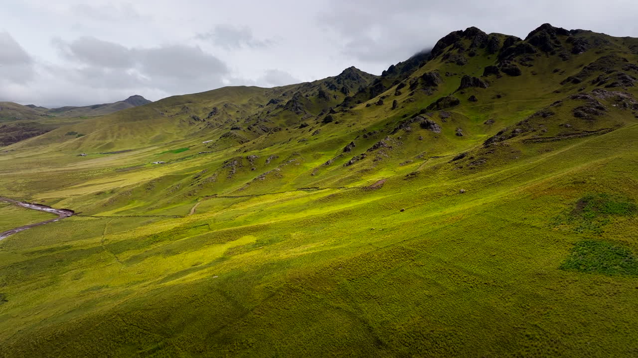 Altipiani andini verdi nel Distretto di Kunturkanki, Provincia di Canas, Cusco, Perù. Pascoli ondulati, crinale roccioso e cielo minaccioso in Sud America, vista aerea cinematografica in movimento.