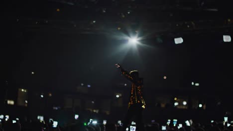 las luces del escenario y la iluminación de los teléfonos inteligentes arrojan un resplandor vibrante en el cantante apasionado que actúa, irradiando energía intensa y emoción durante el electrificante momento de música en vivo