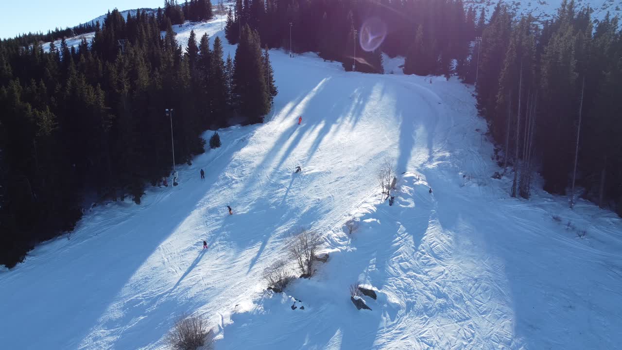 clip aéreo estático de personas esquiando alrededor de la curva de una ladera de montaña al sol en la estación de esquí de vitosha cerca de sofía, bulgaria con un teleférico corriendo en el fondo