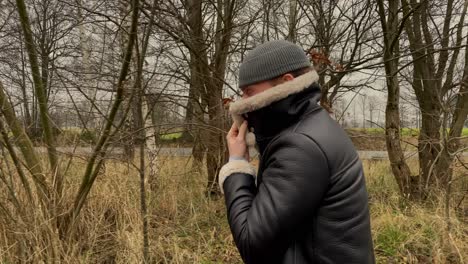 Toma-De-Pista-En-Cámara-Lenta-De-Un-Joven-A-La-Moda-Con-Sombrero-Y-Chaqueta-De-Cuero-Caminando-Al-Aire-Libre-En-La-Naturaleza