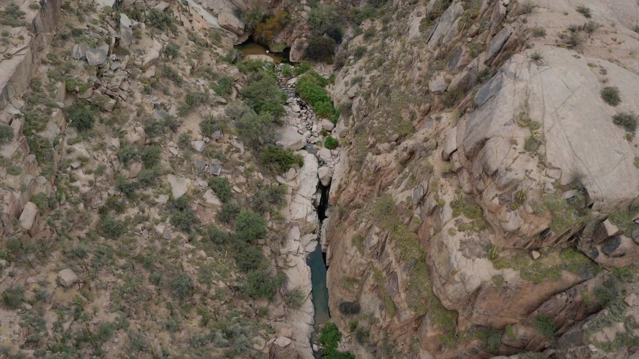 Discesa aerea in un aspro canyon roccioso che rivela una pozza d'acqua isolata all'interno di un paesaggio arido