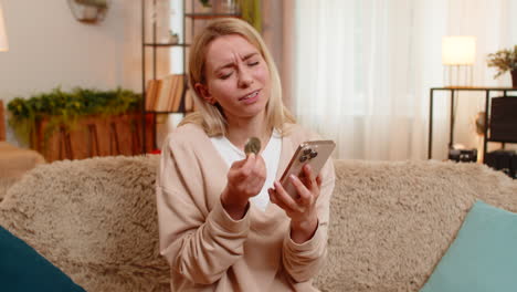 Adult woman checking bitcoin drop on smartphone at home shaking head in disappointment frustration