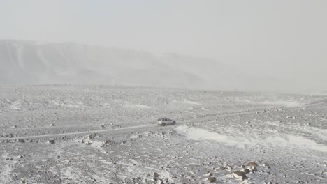 Toma-Aérea-De-Un-Vehículo-Todoterreno-Conduciendo-A-Través-De-Una-Tormenta-De-Nieve-En-El-Desierto-De-Islandia