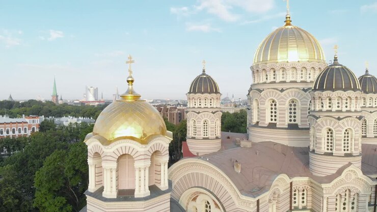 Drone aéreo subindo acima da cúpula dourada da Catedral da Natividade de Cristo, com a paisagem urbana panorâmica revelada ao fundo, em um dia ensolarado.