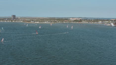 Drohne---Luftaufnahme-Vieler-Surfer-Auf-Einem-Blauen,-Welligen-Und-Windigen-Meer-An-Einem-Sonnigen-Tag-Mit-Weißen-Wolken-Auf-Einer-Insel,-Zeeland,-Niederlande,-30p