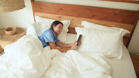 woman in bed laughing while holding smartphone, enjoying morning relaxation, at home