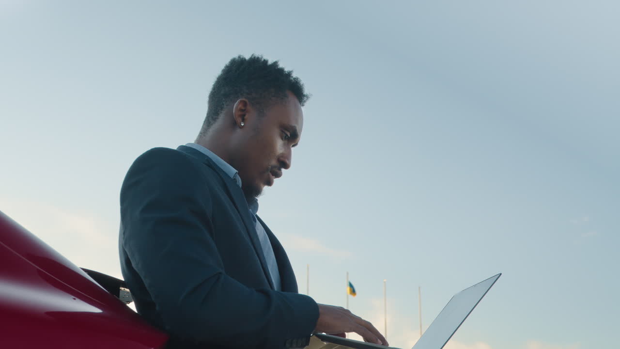 충전소 에서 전기 자동차 근처 의 노트북 에서 일 하는 사업가