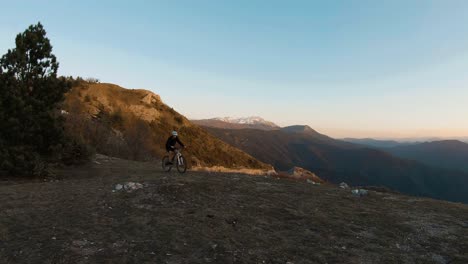 young man riding a bike at the top of a mountain at sunset