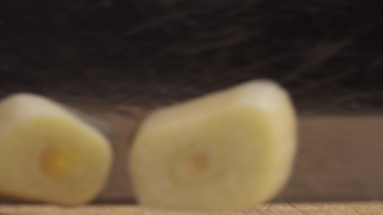 Person cutting garlic in wooden board. Macro close-up