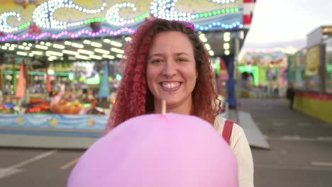 happy woman smiles at camera with cotton candy and fair background