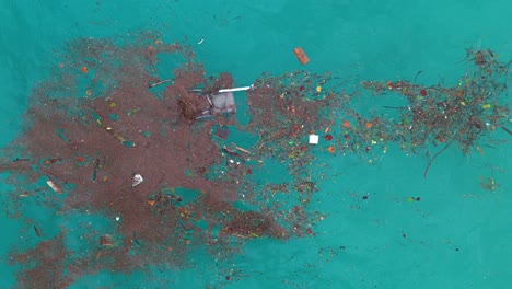 aerial overview of garbage pathc of red plastic and broken chairs mixed with natural fibers in blue ocean water