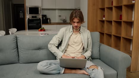 hombre relajado sentado en el sofá trabajando desde casa en una computadora portátil