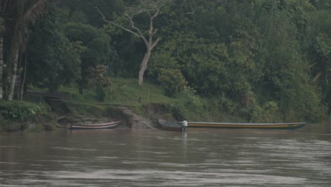 Hombre-Amarrando-Un-Barco-De-Madera-En-La-Orilla-Del-Río-Amazonas---Ancho