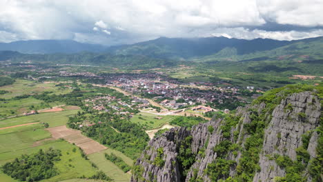 Aerial flyover cliff edge to reveal farmlands in Vang Vieng Laos, revealing misty distant hills