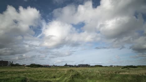 timelapse de nubes moviéndose hacia el espectador en un cielo azul sobre casas con gras en primer plano