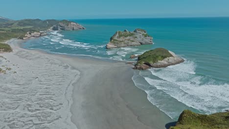 reverse aerial revealing picturesque view of unique rock formation outcrops at popular tourist destination of wharariki beach at cape farewell in nelson, south island of new zealand aotearoa