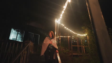 woman standing on a wooden staircase at night, illuminated by string lights