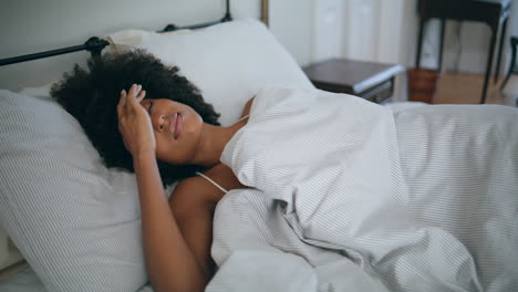 Drowsy-model-awaking-at-bed.-Curly-hairstyle-sleepy-woman-hiding-under-blanket