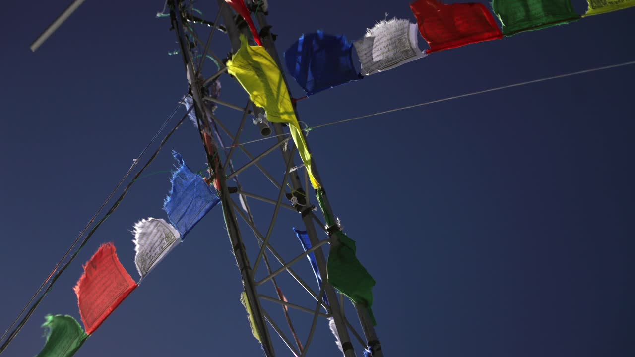 Aspen Highlands bowl blue bird sky sunny winter spring day close up Nepali prayer flags metal pole Colorado Snowmass Elk Mountains morning afternoon no clouds top of peak pan left motion