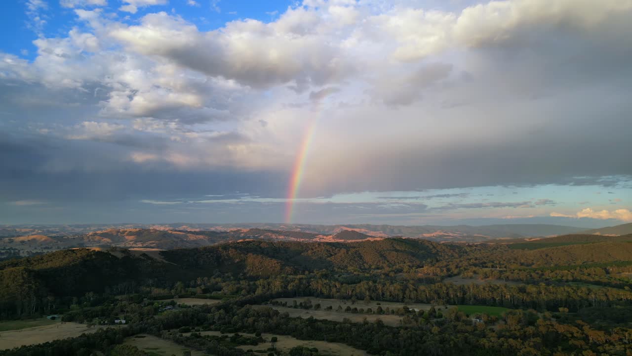 Beautiful rainbow drone shot in countryside with mountain range in background