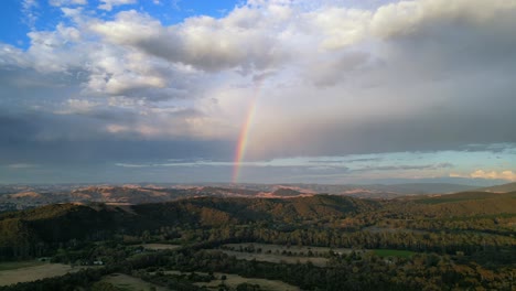 beautiful rainbow drone shot in countryside with mountain range in background