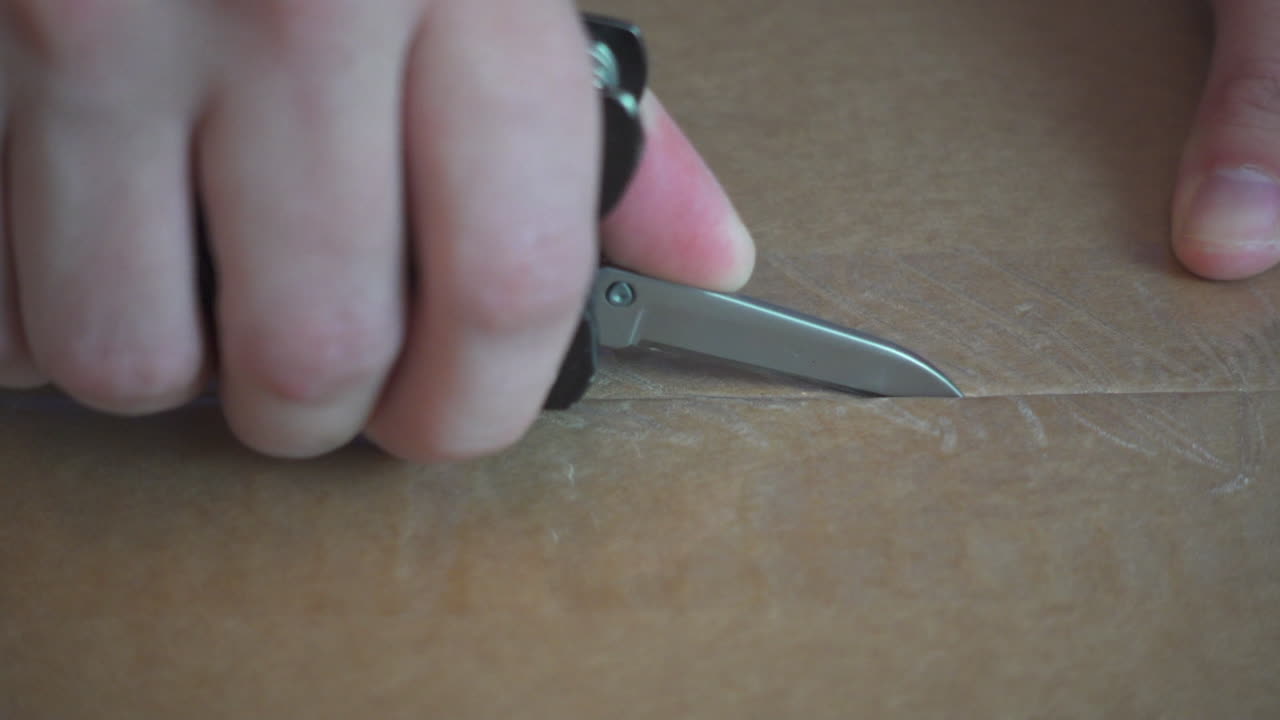 Scena ravvicinata del taglio di una scatola di spedizione in cartone con un attrezzo multiuso. Perfetto per progetti di magazzino, spedizione e logistica.
