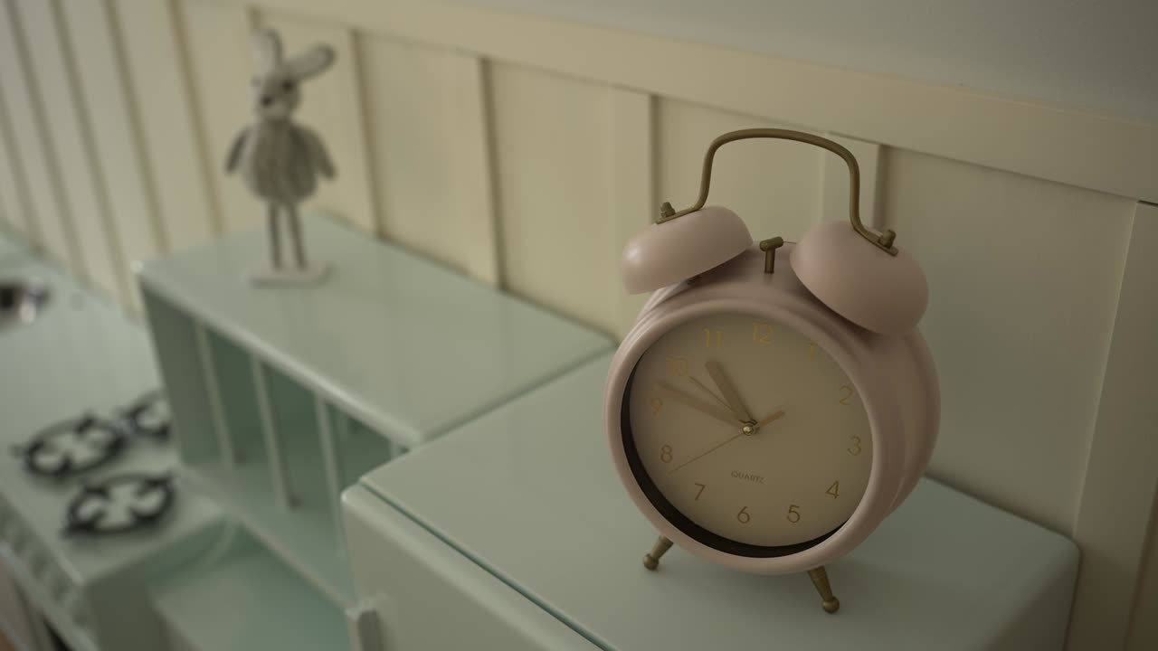 Close up of a pastel pink alarm clock placed on a light cabinet indoors
