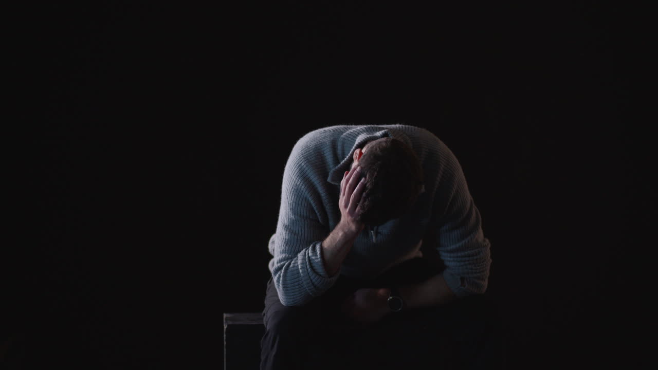 Sad man sitting with hands on his head in a dark room