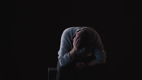 sad man sitting with hands on his head in a dark room