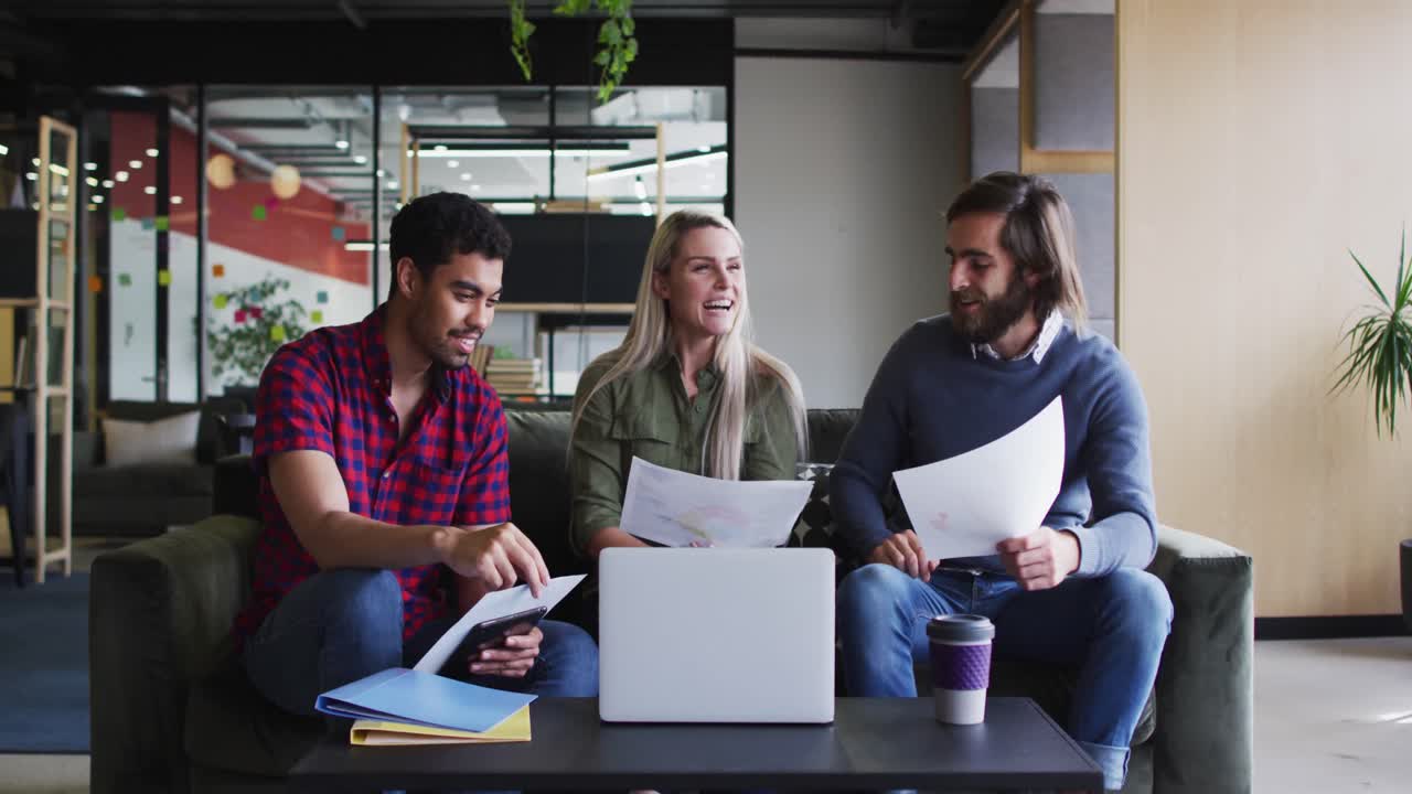 Diverse business people sitting using laptop and goign through paperwork in modern office