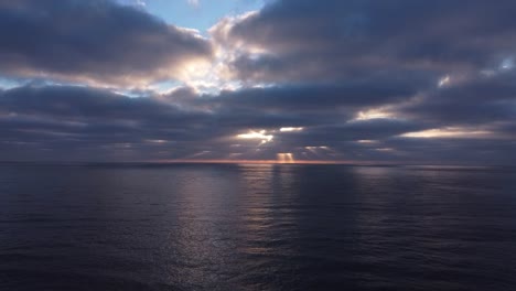 vista de drones de los rayos del sol alcanzando su punto máximo a través de espesas nubes oscuras sobre el océano por la noche