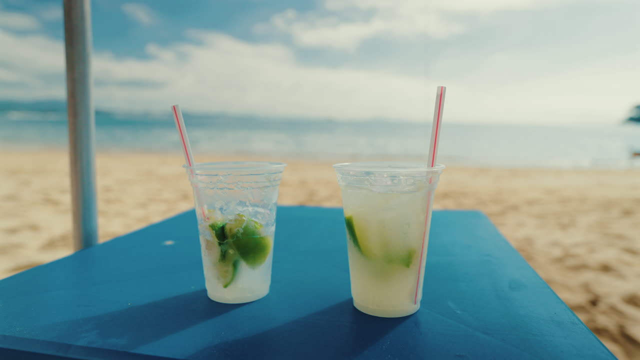 Close-up view of Caipirinha what is a traditional Brazilian refreshing cocktail on a blue table with sandy beach and playing dogs