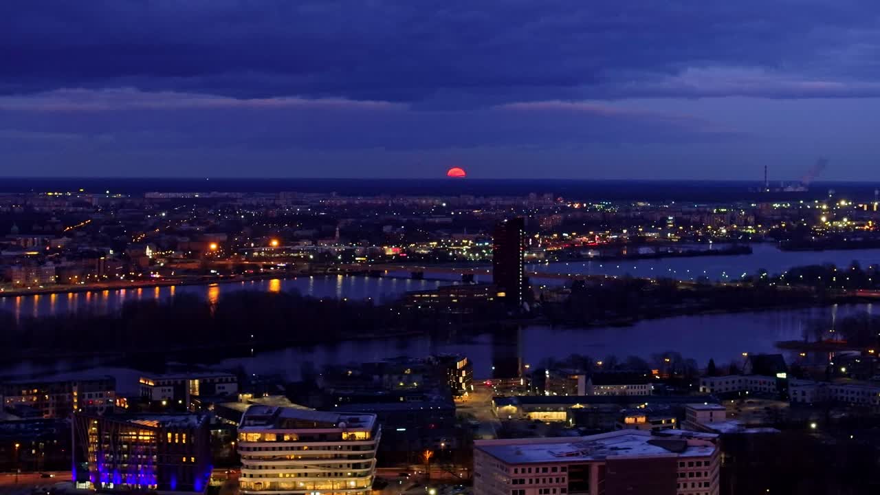 Left pan shows huge orange moon rising above Riga skyline during lunar eclipse