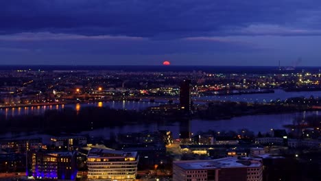 left pan shows huge orange moon rising above riga skyline during lunar eclipse