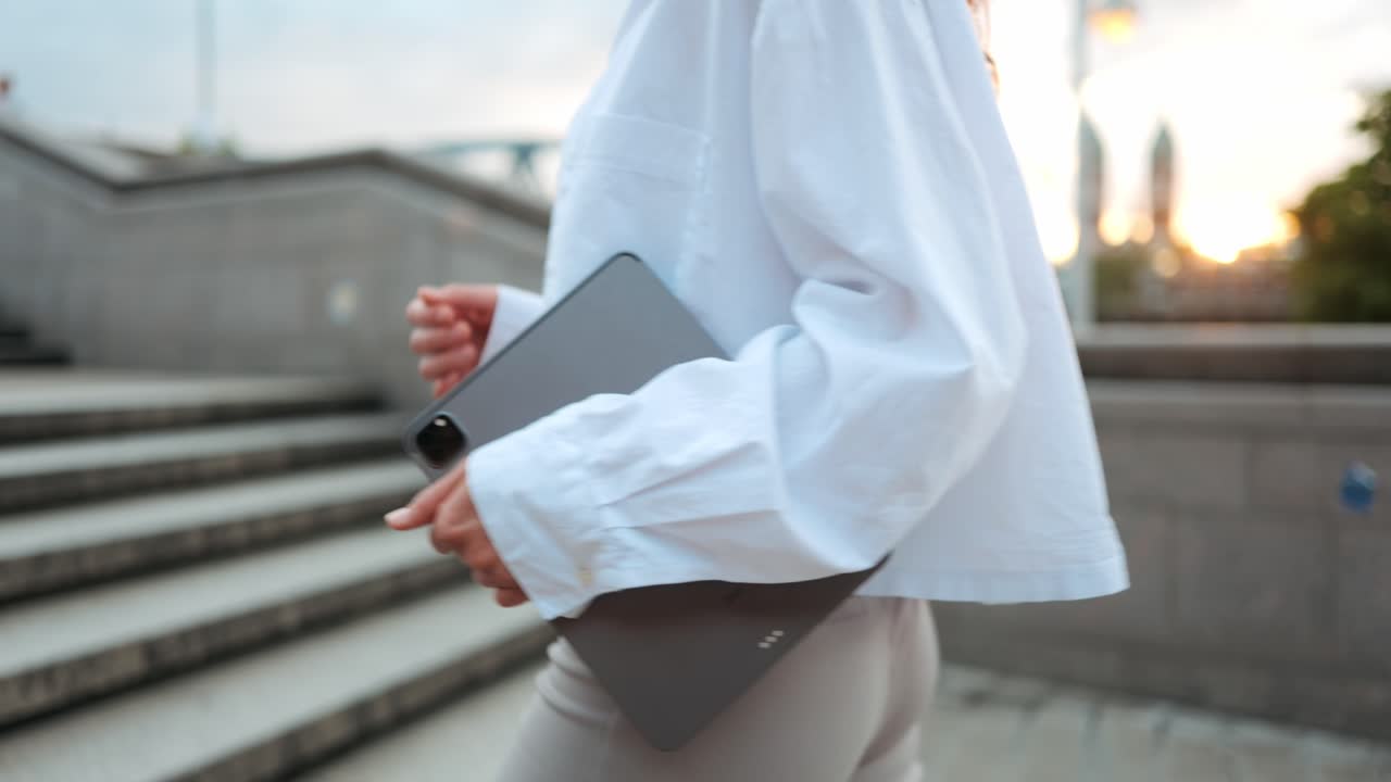 Modern young businesswoman with tablet walk up stairs against urban background, concept career advancement female empowerment