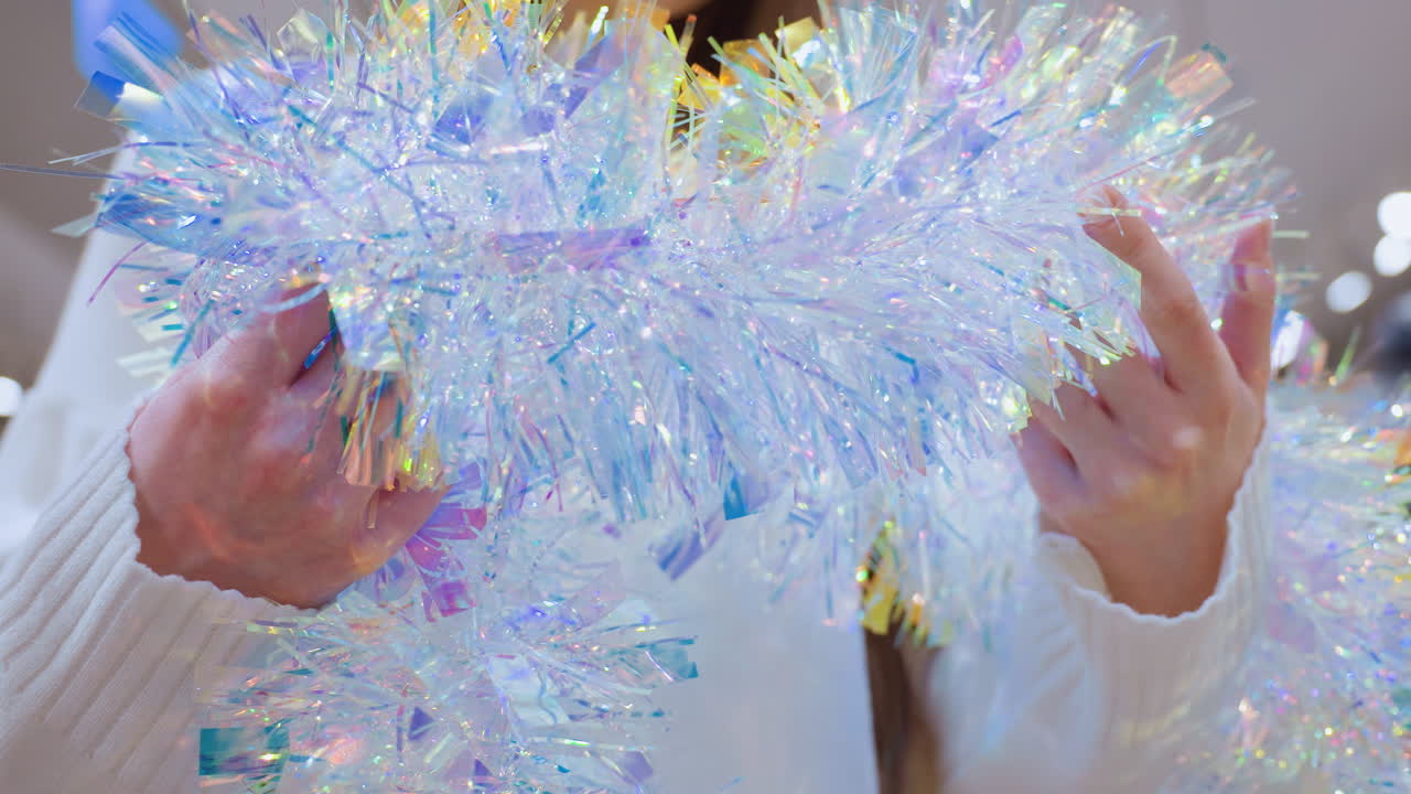 Close-up of female shopper holding shimmering tinsel and observing it thoughtfully in a decor store with bokeh lights in the background