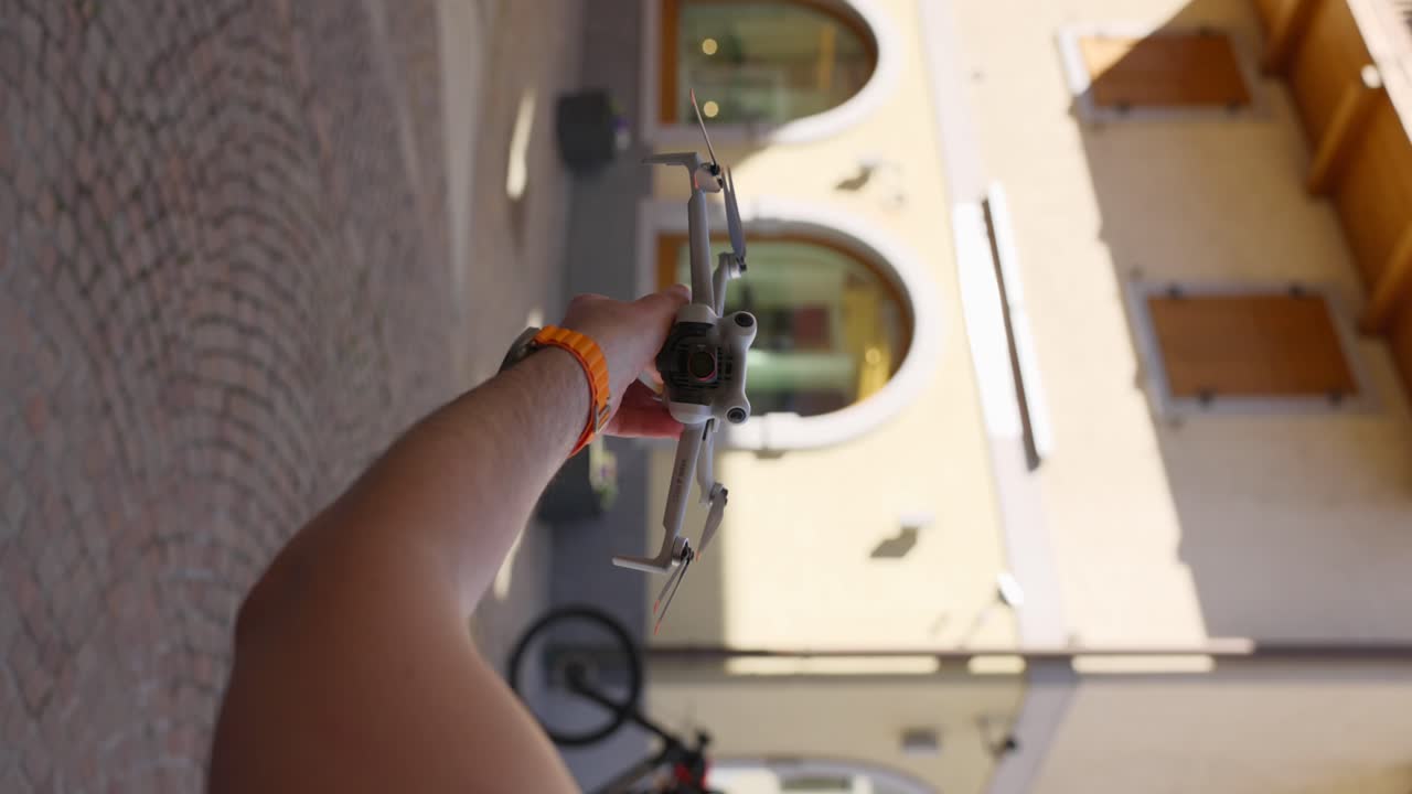Pov view of a person launching a drone in a sunny urban courtyard, Showcasing modern technology and outdoor adventure