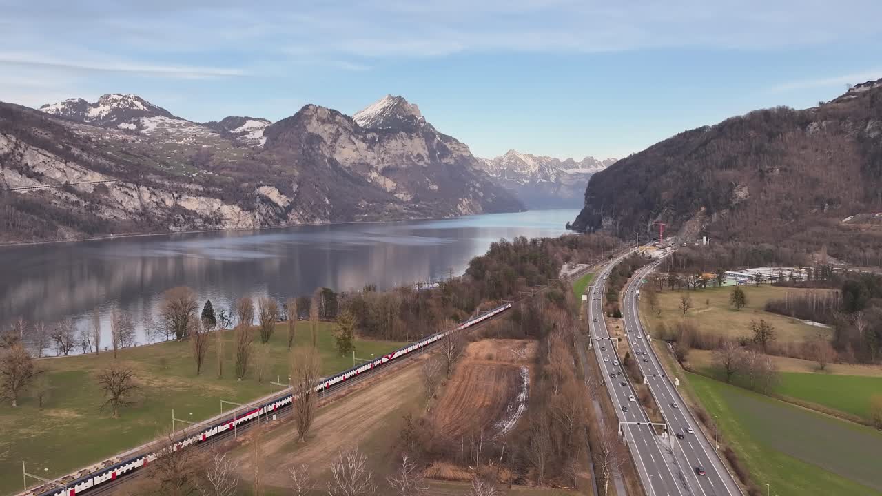 Aerial - train and highway running parallel to Walensee lake with Swiss Alps in Switzerland